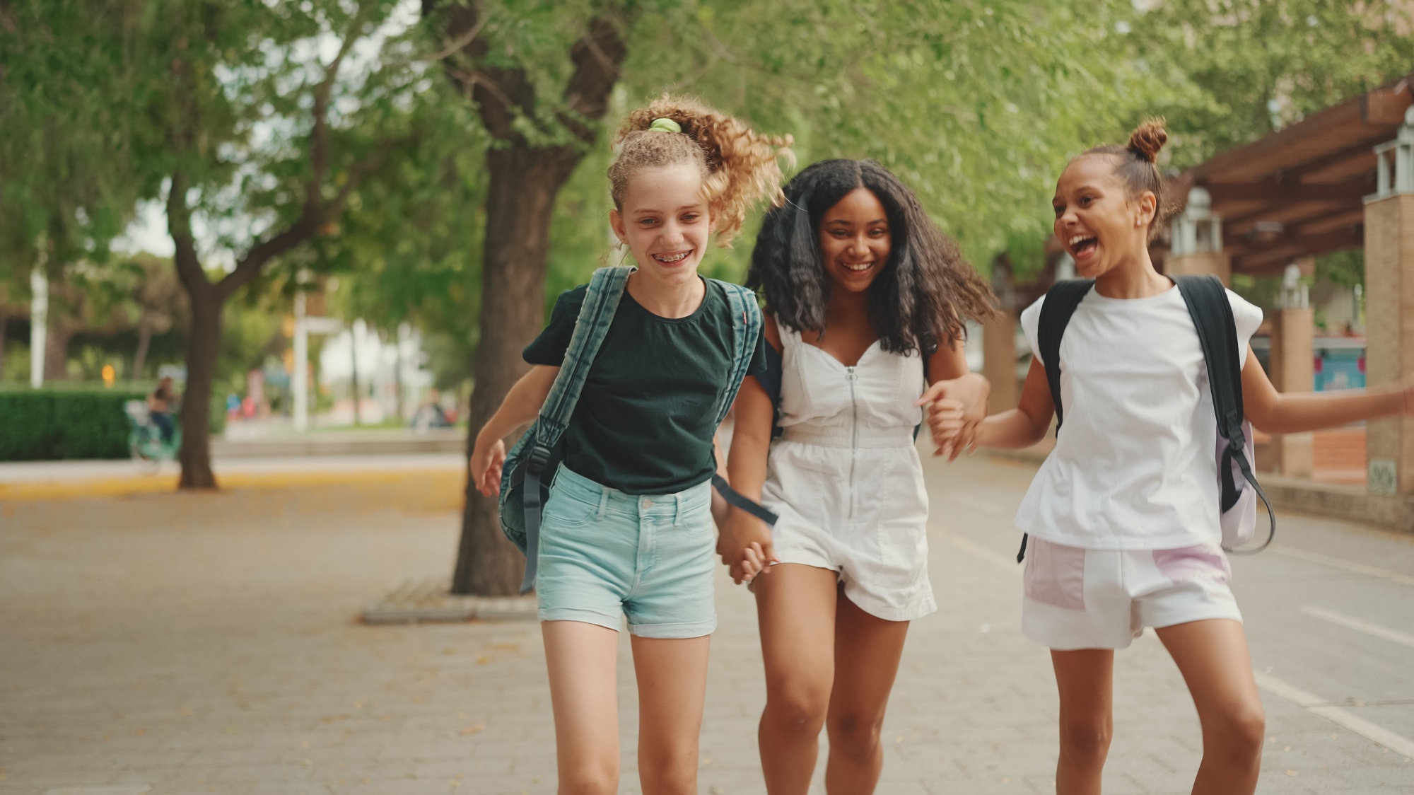 Three girls friends pre-teenage dance and play in the city park background